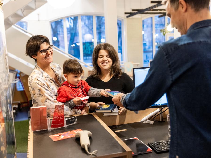 Familie afleverer bøger til bibliotekar. Foto: Nikolai Linares. Centralbibliotekernes Fotobank.