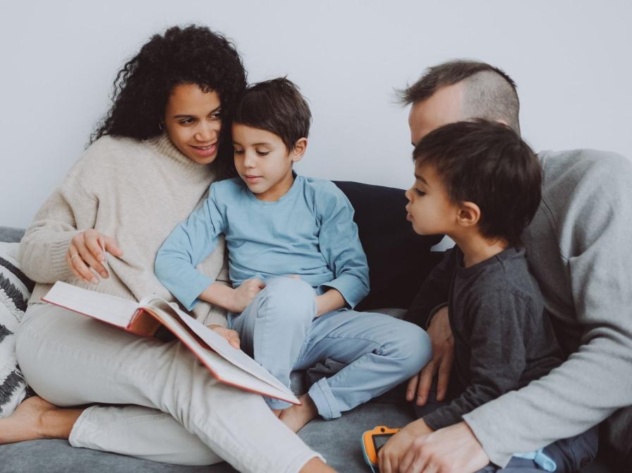 Familie sidder sammen i sofaen og læser en bog højt.